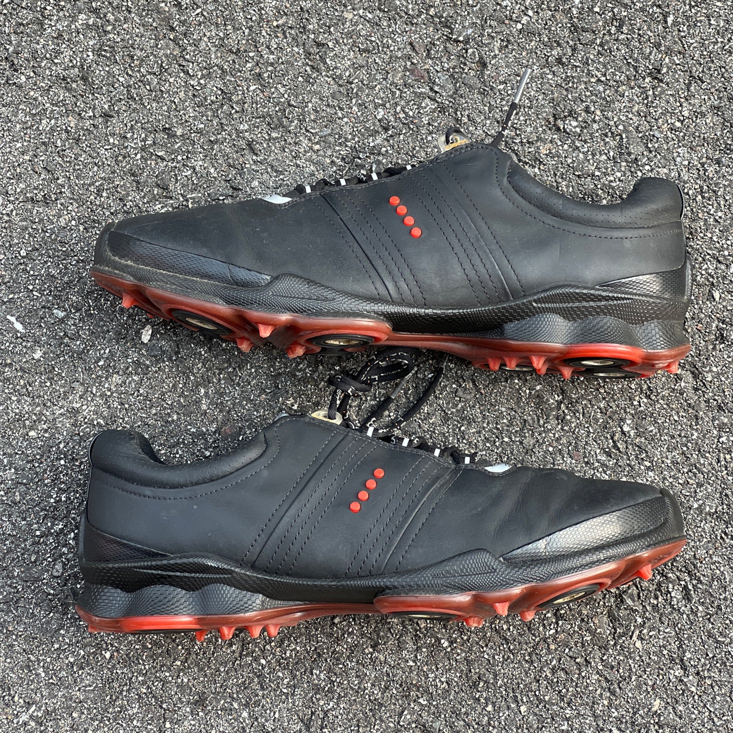 Black athletic shoes with red accents on a gray asphalt surface